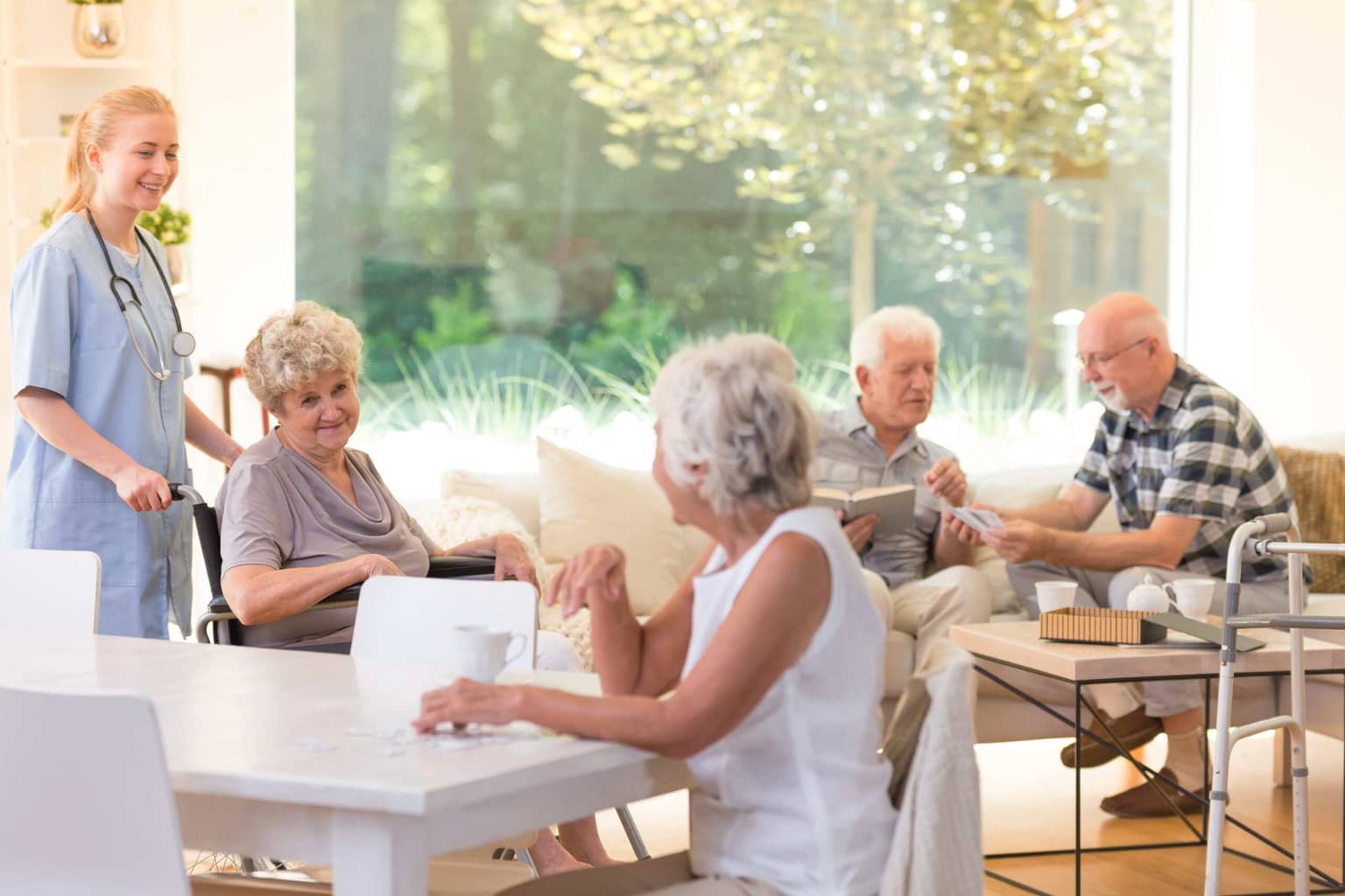 Seniors socializing and reading in a bright assisted living common area.